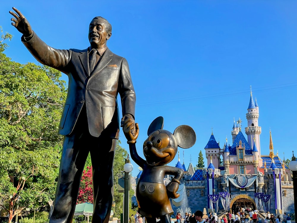 a statue of walt and mickey mouse in front of a castle