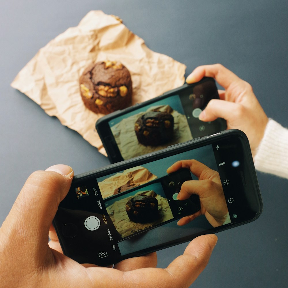 two people taking pictures of pastries on their cell phones