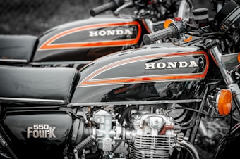 Two vintage motorcycles with the brand name 'HONDA' prominently displayed on the gas tanks. The motorcycles have a distinctive black and orange color scheme, with chrome and metal engine parts visible.
