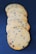 Five chocolate chip cookies are arranged in a slightly overlapping line, set against a dark blue background. The cookies have a golden-brown color with visible chocolate chips embedded in them, indicating they are freshly baked.