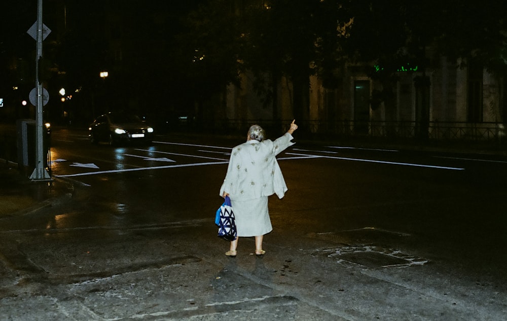 a woman in a white coat crossing a street at night