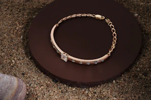 A stylish gold bracelet laid out on a marble surface with natural light highlighting its texture.