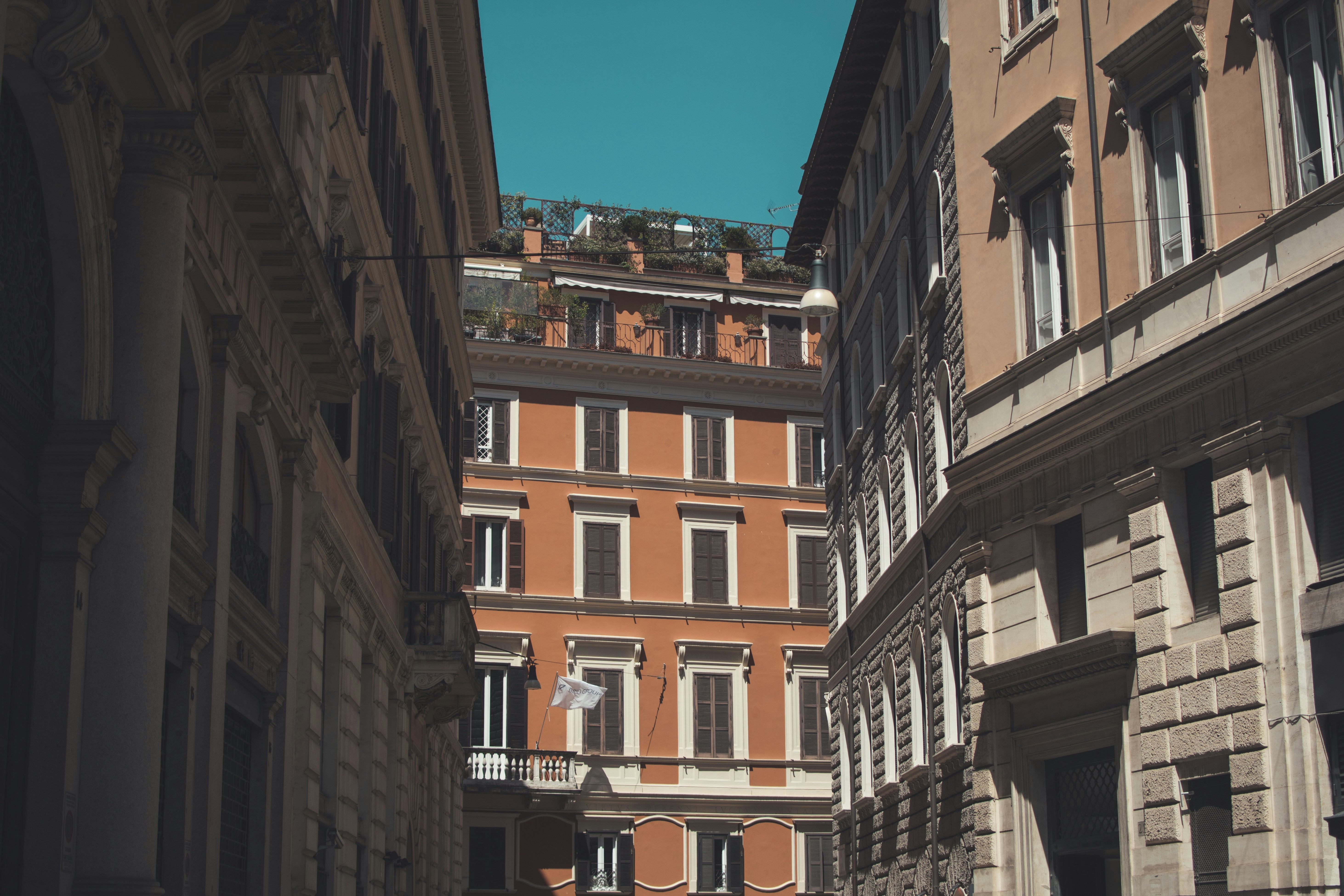 a narrow street in a city with tall buildings, Looking up in the streets of Rome