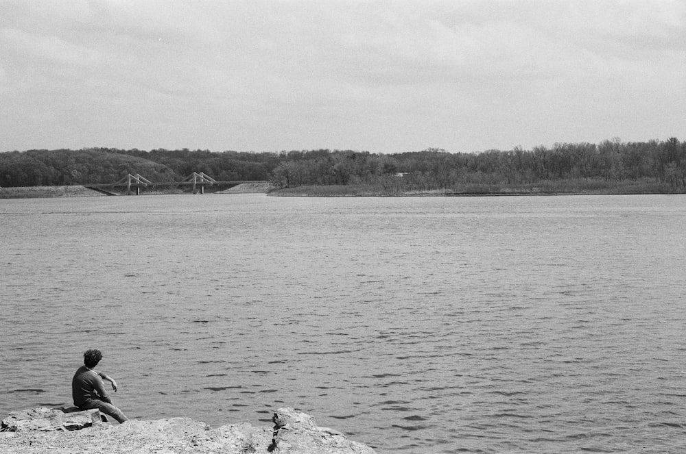 a man sitting on a rock near a body of water