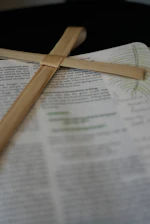 Close-up of an open Bible with highlighted verses and a wooden cross resting on the page.