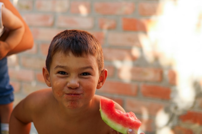 A cheerful child biting into a juicy apple with sunlight streaming in the background.