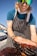Photo of a smiling chef holding fresh meat cuts in a busy restaurant kitchen.