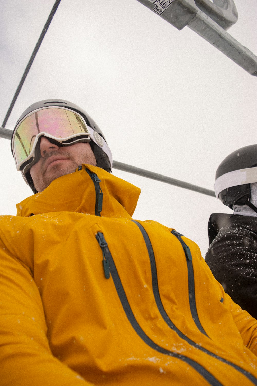 a man in a yellow jacket and goggles on a ski lift