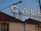 A large sign featuring the word 'CALE' is placed on top of a building with a tiled roof. A construction crane is visible in the background against a clear blue sky. Part of the building facade shows an arched window.