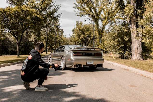 Professional car photographer taking pictures of a sleek vehicle in front of a modern home.