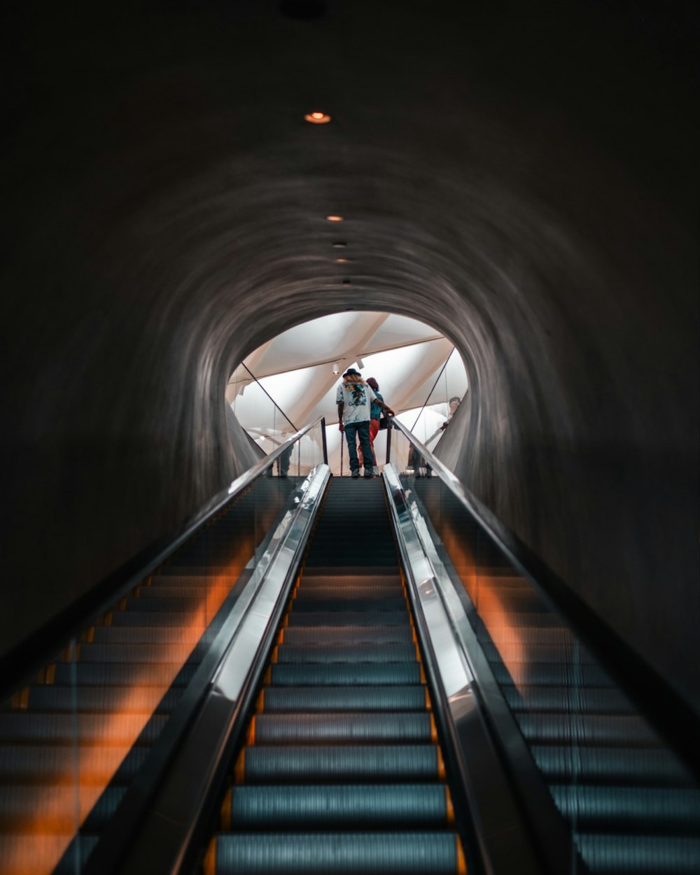 deux personnes debout sur un escalator dans un tunnel