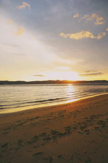 the sun is setting over the water on the beach