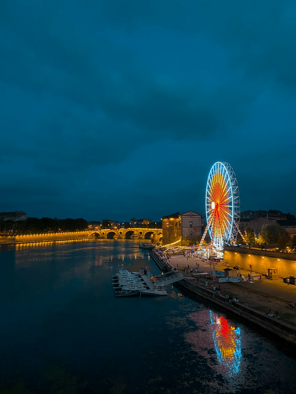 a ferris wheel sitting next to a river under a cloudy sky
