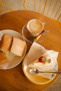 A cozy café table with a cup of espresso, a fresh juice, and a sandwich on a wooden surface.