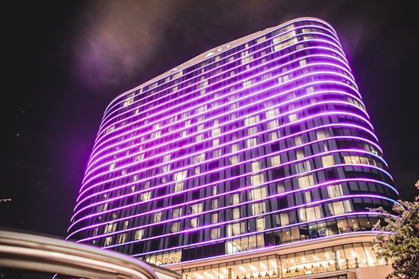 A sleek hotel exterior lit up in purple hues during the evening.