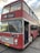 A vintage double-decker bus painted in a faded red color with white accents. The bus is labeled with the route number 025 and has 'Bristol' displayed on the sign above the windshield. The front features classic round headlights and a distinctive grille. The vehicle is parked and its door is open, showing a glimpse of the interior.