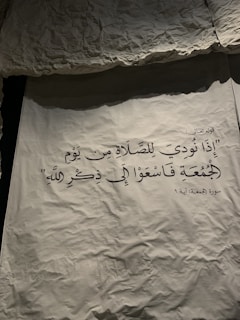 Arabic calligraphy is displayed on a textured, crumpled surface. The text is elegantly written, and there is a contrast between the dark letters and the lighter background.