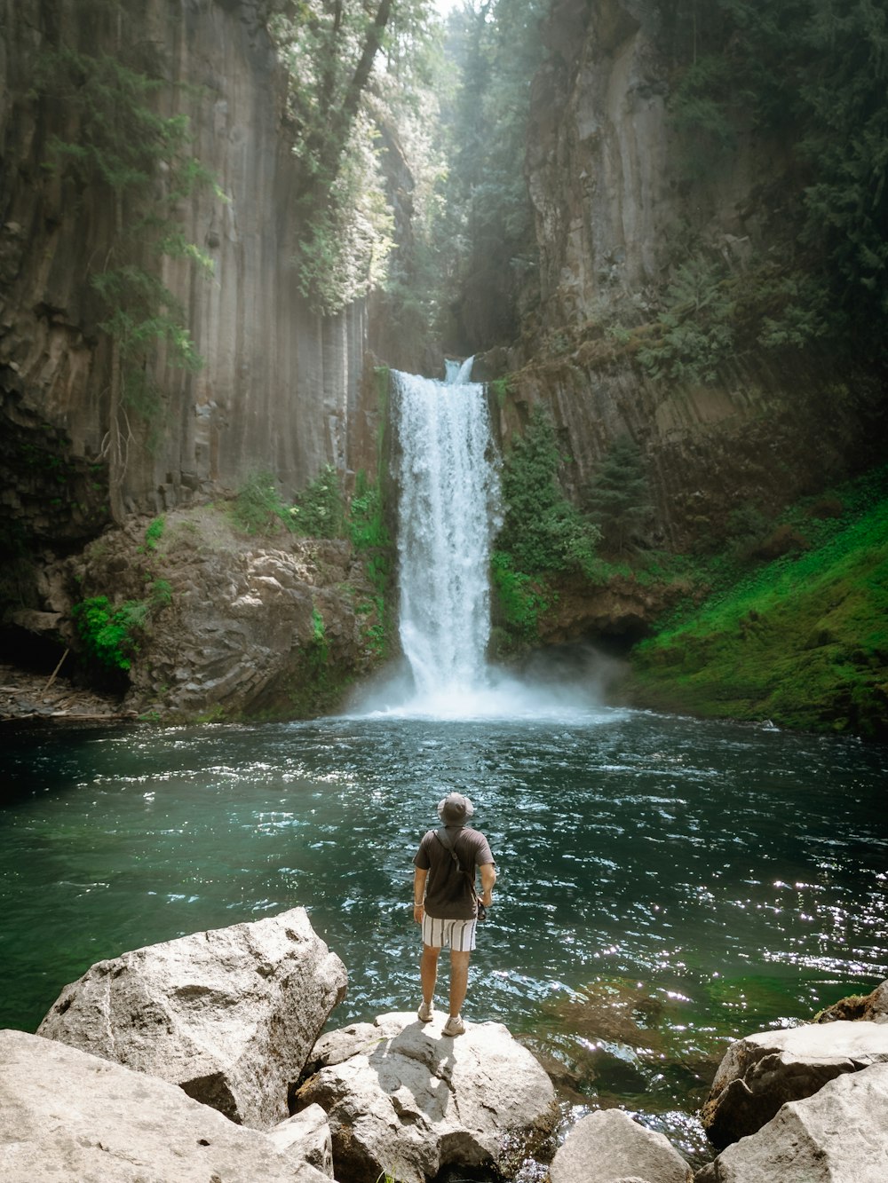 a person standing on a rock in front of a waterfall