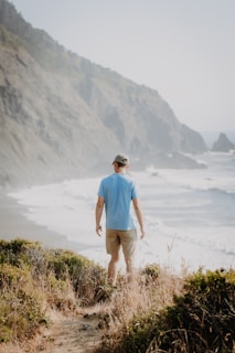 Man in comfortable linen shorts and a casual shirt, standing by turquoise waves on a sunny day.