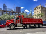 a red dump truck driving down a street next to tall buildings