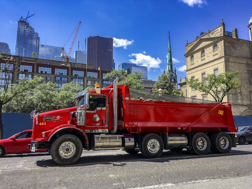 a red dump truck driving down a street next to tall buildings