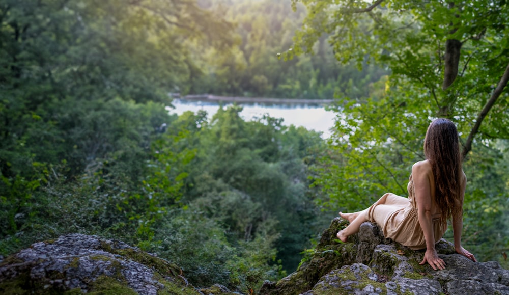 a woman sitting on top of a rock next to a forest