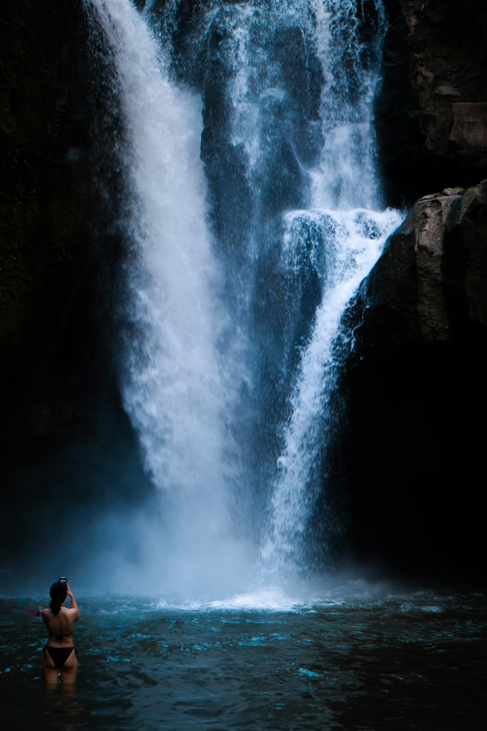 a person standing in a body of water near a waterfall