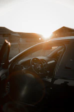 A professional driver opening the door of a sleek black luxury car against a Dubai city skyline at sunset.
