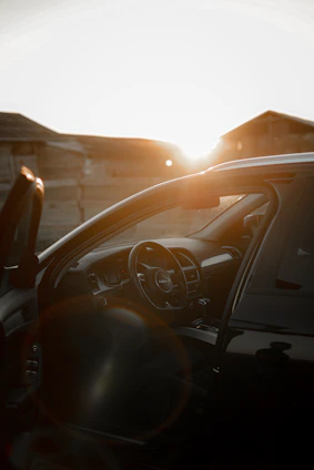 A professional driver opening the door of a sleek black luxury car against a Dubai city skyline at sunset.