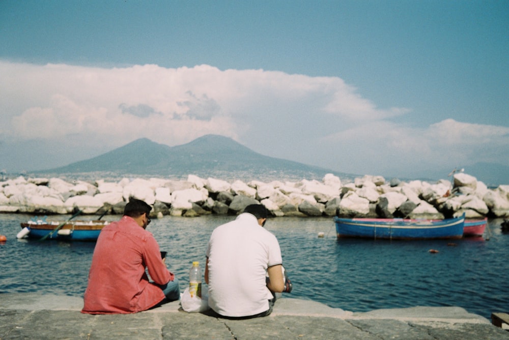 Un par de personas sentadas en una roca junto a un cuerpo de agua