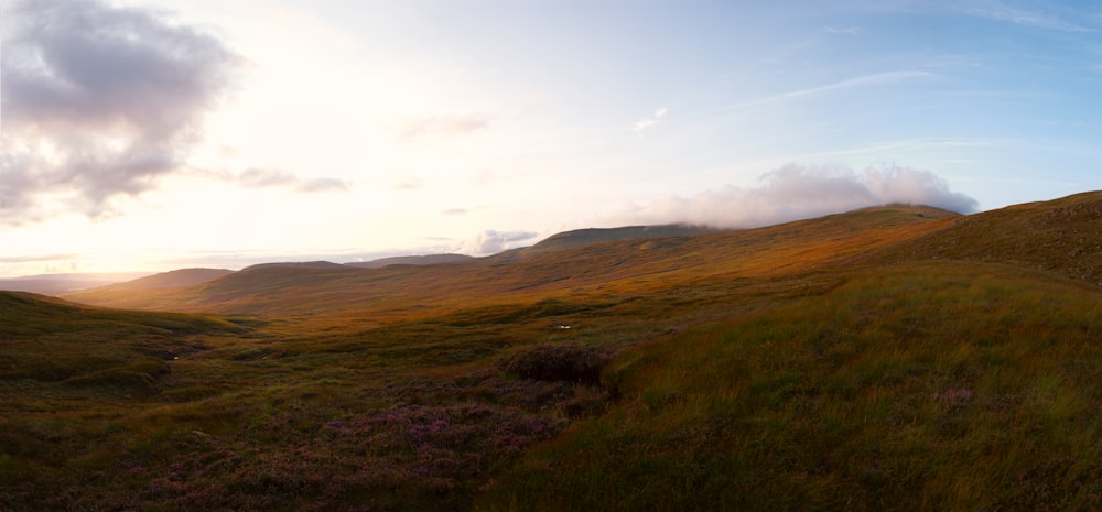 a grassy hill with a few clouds in the sky