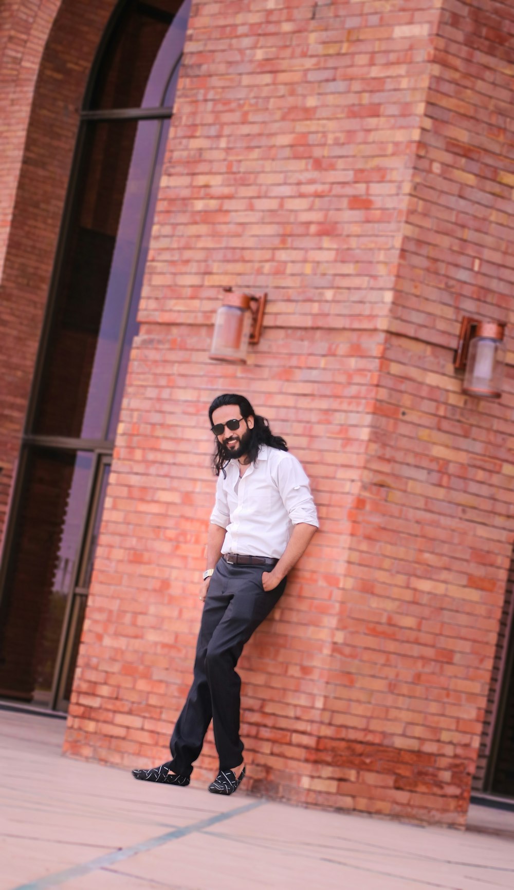 a man with long hair and a beard leaning against a brick wall