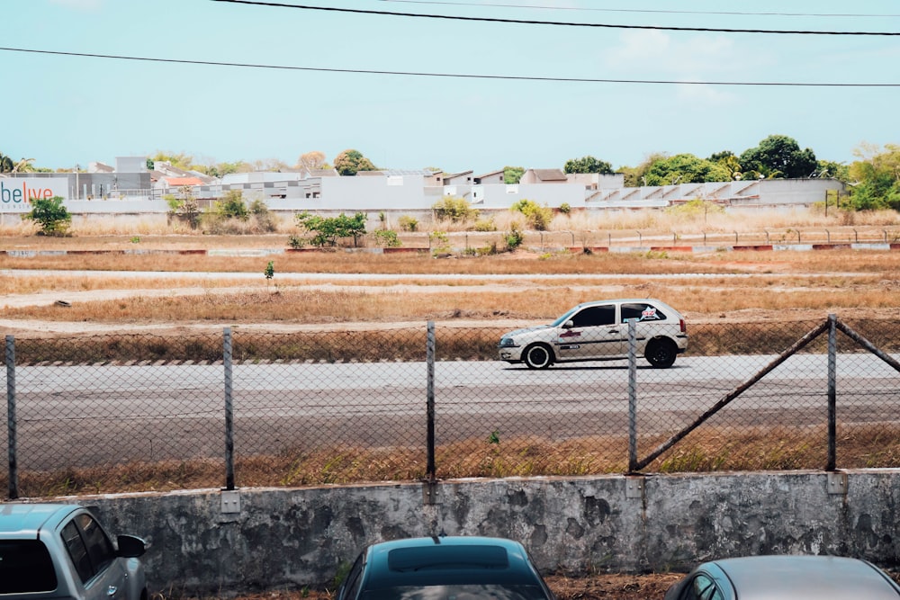 a white car driving down a street next to a fence