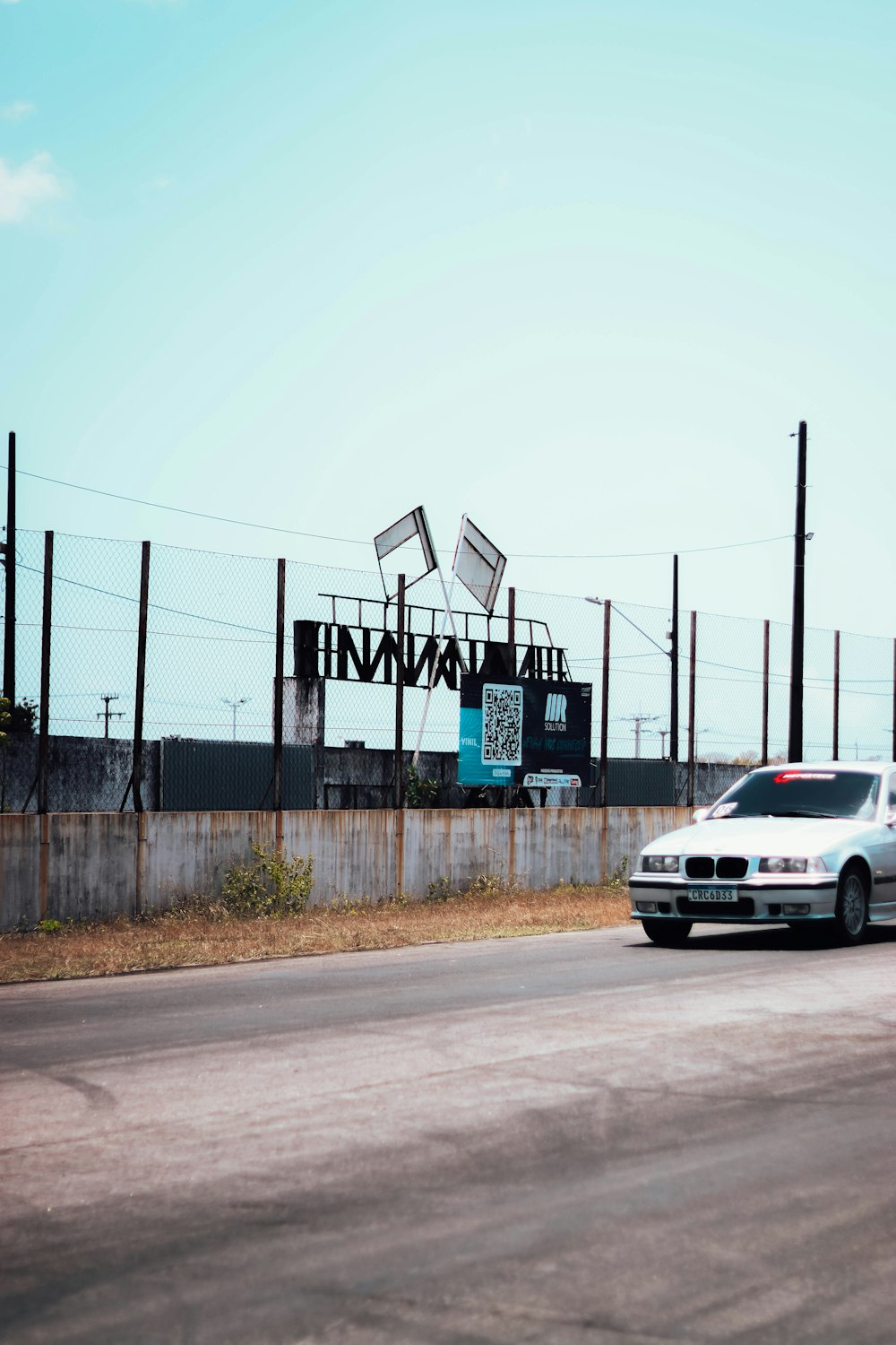 a white car driving down a street next to a fence