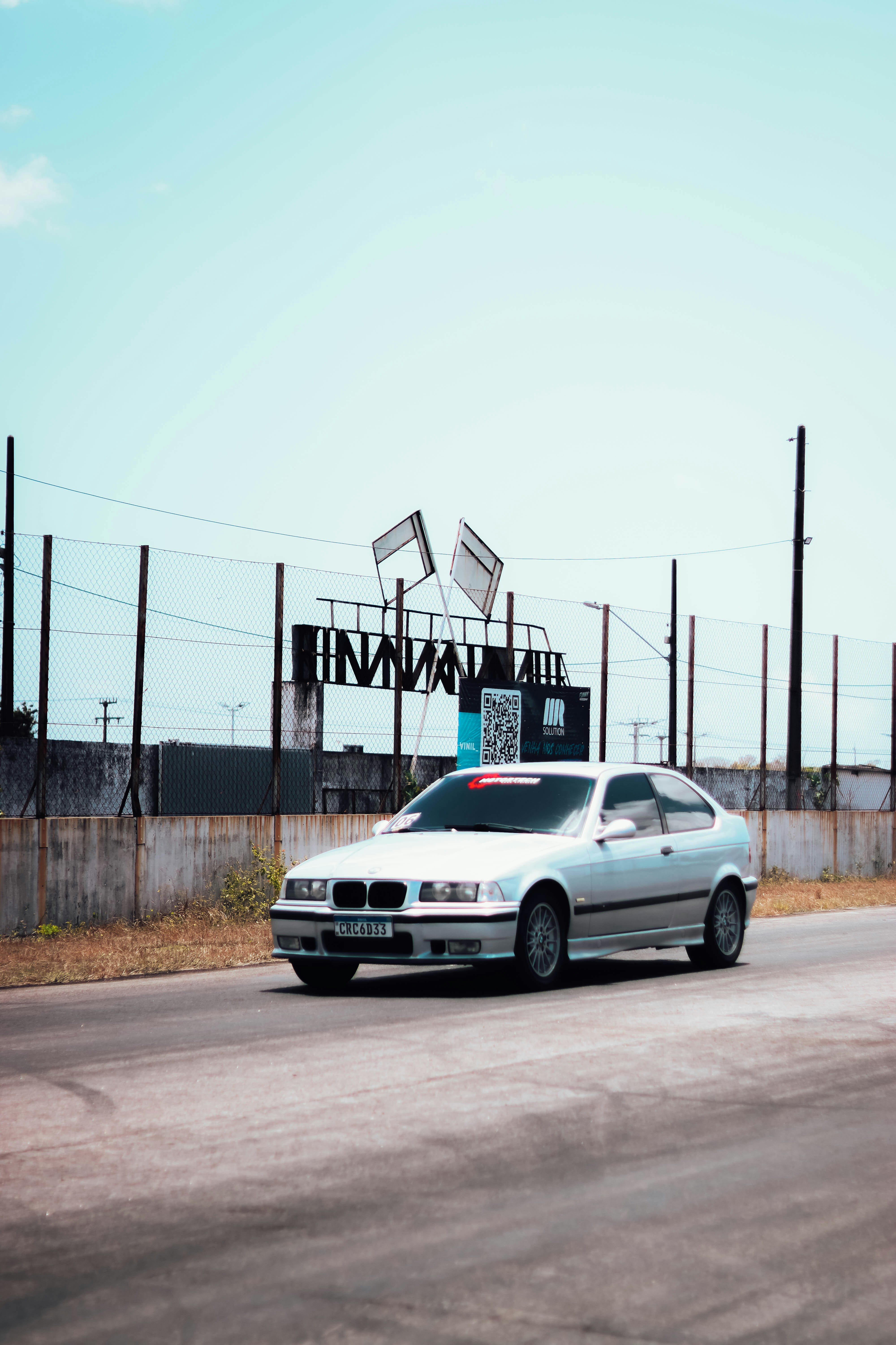 a silver car driving down a street next to a fence