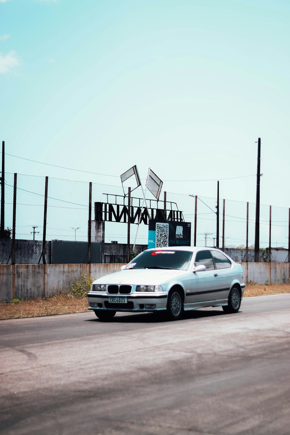 a silver car driving down a street next to a fence