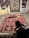 A person is kneeling next to a collection of intricately designed Persian rugs with vibrant patterns and colors. The rugs are displayed on a stone floor and hanging on doors, each showcasing a variety of geometric and floral motifs.