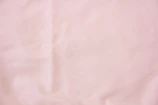 Soft blush pink abstract texture with gentle folds and shadows, evoking luxury fabric.