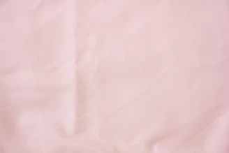 A delicate blush pink fabric swatch layered softly with warm sand and gentle taupe textiles.