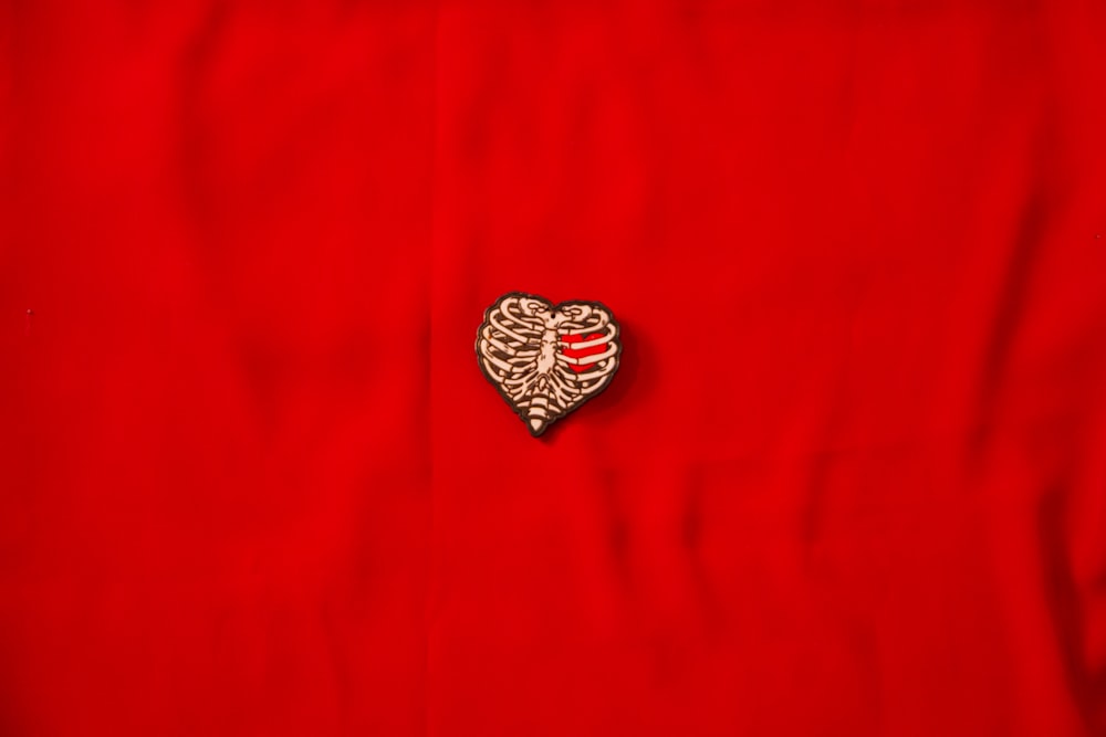 a heart shaped brooch sitting on top of a red cloth