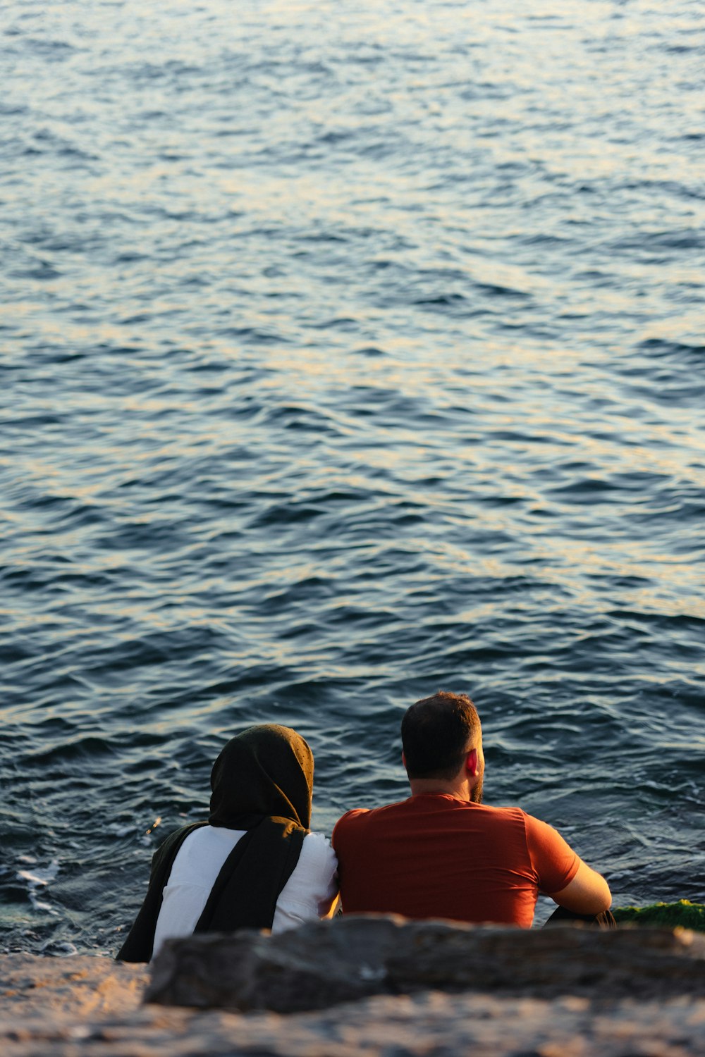 a couple of people sitting on top of a beach next to a body of water