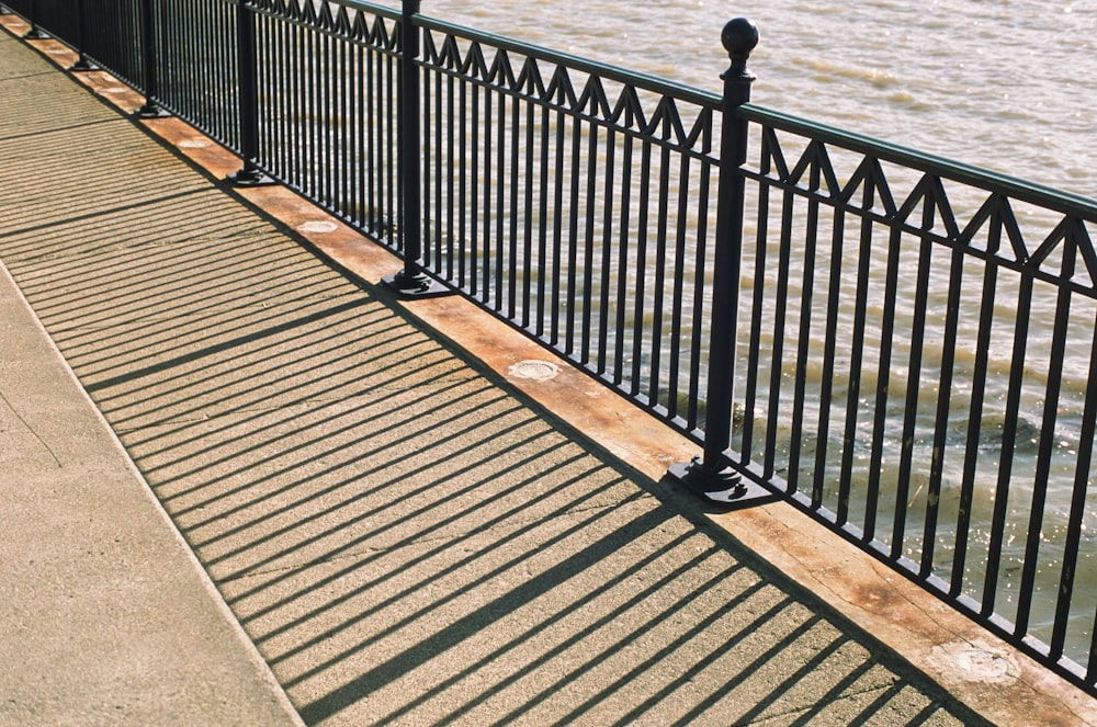 a bench sitting next to a metal fence near a body of water