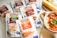 A selection of Denny sauce packets is displayed alongside a bowl of curry with rice and a rolled flatbread on a plate. The packets are flavors like Chicken A La King, Curry Sauce, and Stroganoff, among others. The curry in the bowl has a rich orange sauce garnished with fresh coriander.