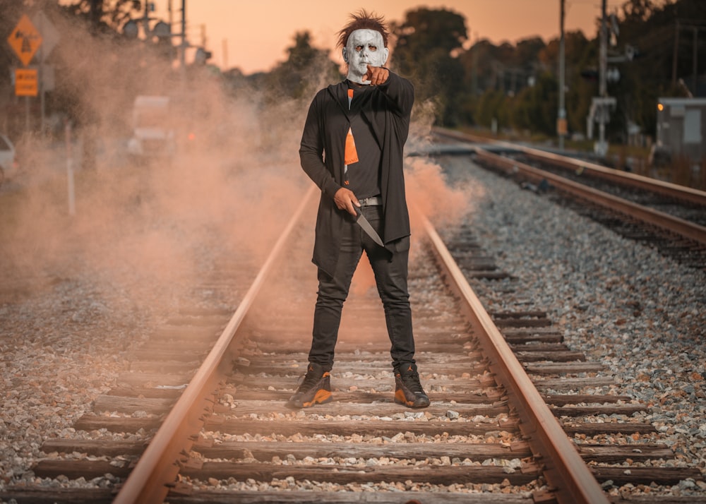 a man wearing a mask standing on train tracks