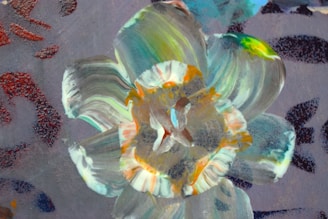 A vibrant and colorful abstract painting with swirling patterns and shapes. The composition features a blend of green, orange, and blue hues with prominent brush strokes creating a dynamic flower-like motif against a textured background.