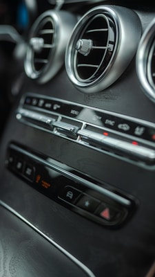 Close-up of a car's interior dashboard featuring two circular air vents with metallic trims and various control buttons below.