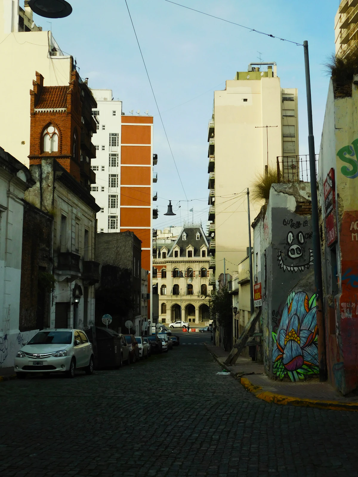 A cobblestone San Telmo street with old facades, a mural-covered wall and a mansard-roofed building at the end