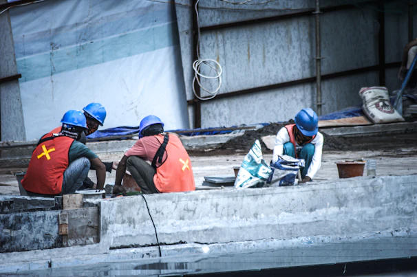 Workers in orange helmets and black uniforms collaborating on a concrete foundation.