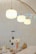 A modern kitchen counter features minimalistic decor with glass jars and a coffee grinder. Three pendant lights hang above, casting a warm glow. The background showcases glossy, iridescent tiles in neutral tones, adding texture and subtle color shifts.