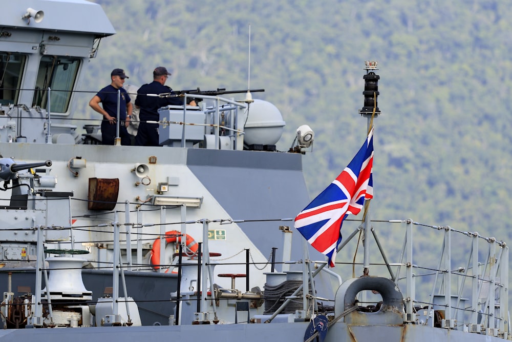 two men standing on top of a boat with a flag